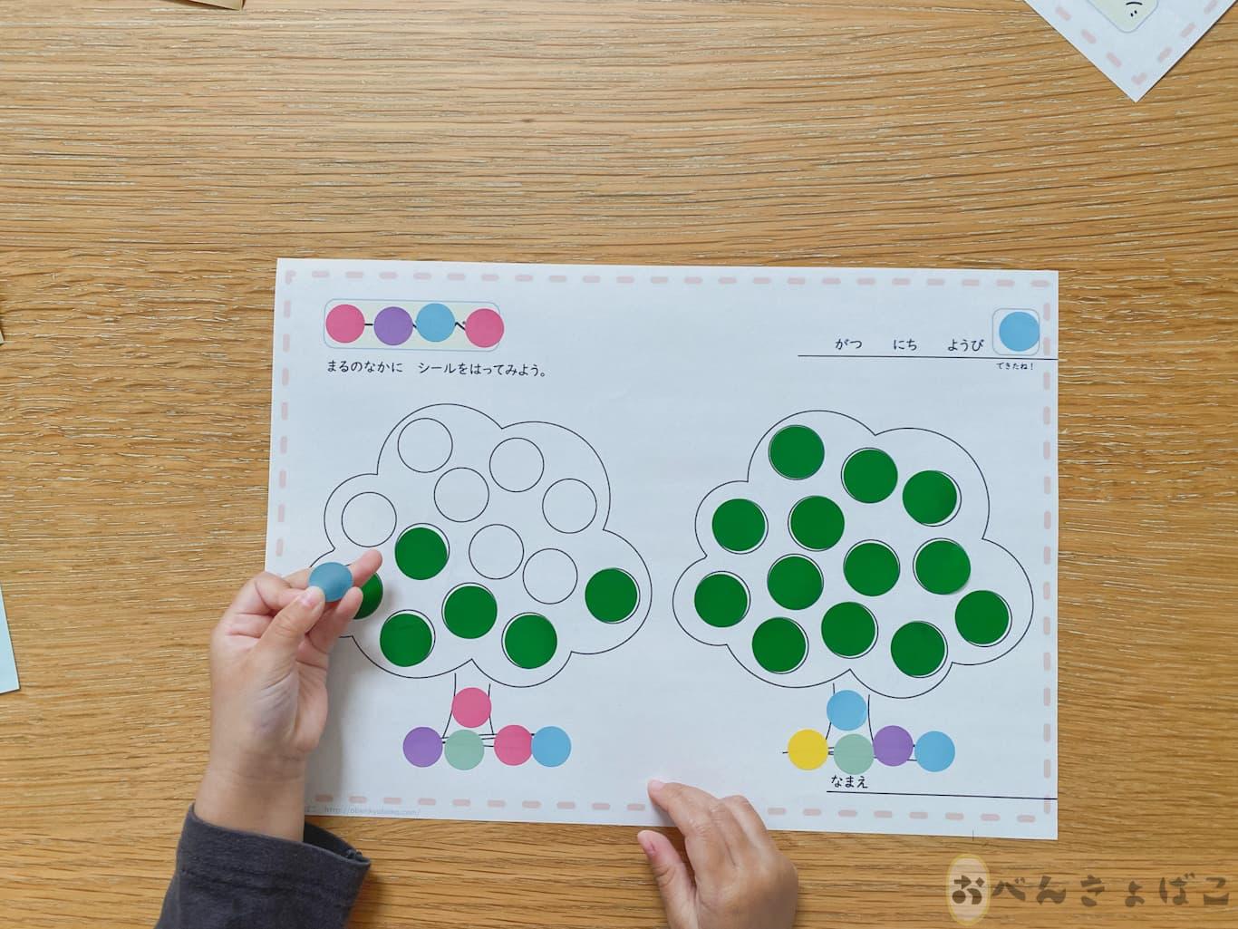 子どもが知育プリントに丸いシールを貼っている手
